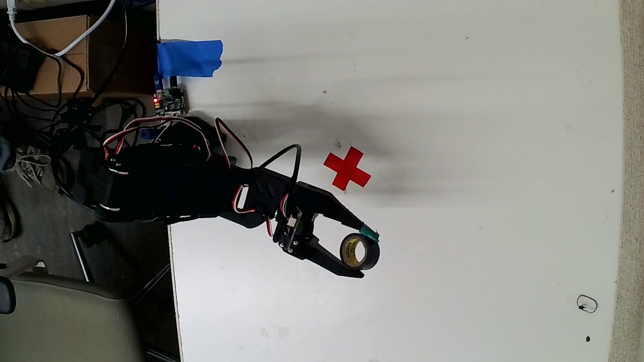 SO-101 robot arm holding a roll of tape over its workbench